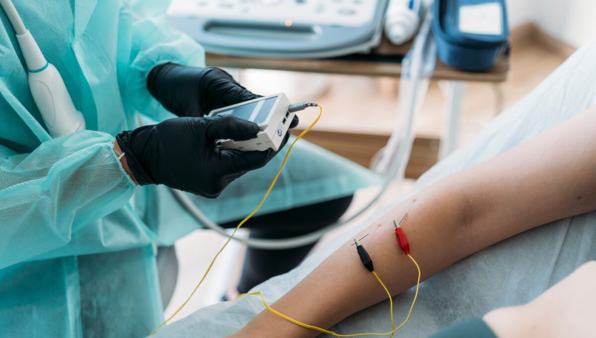 Doctor,Wearing,Protective,Clothes,Examining,Woman's,Arm,With,Electrodes